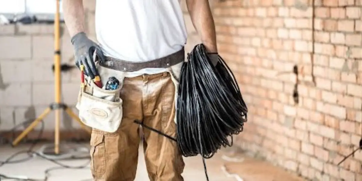 A professional electrician wearing work gloves and a tool belt stands in a construction area, holding a coiled bundle of electrical cables, ensuring safety during the home renovation.