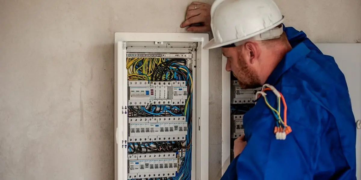 A professional electrician wearing a hard hat and blue protective clothing inspects a breaker panel with multiple wires and circuit breakers, ensuring safety during the home renovation.