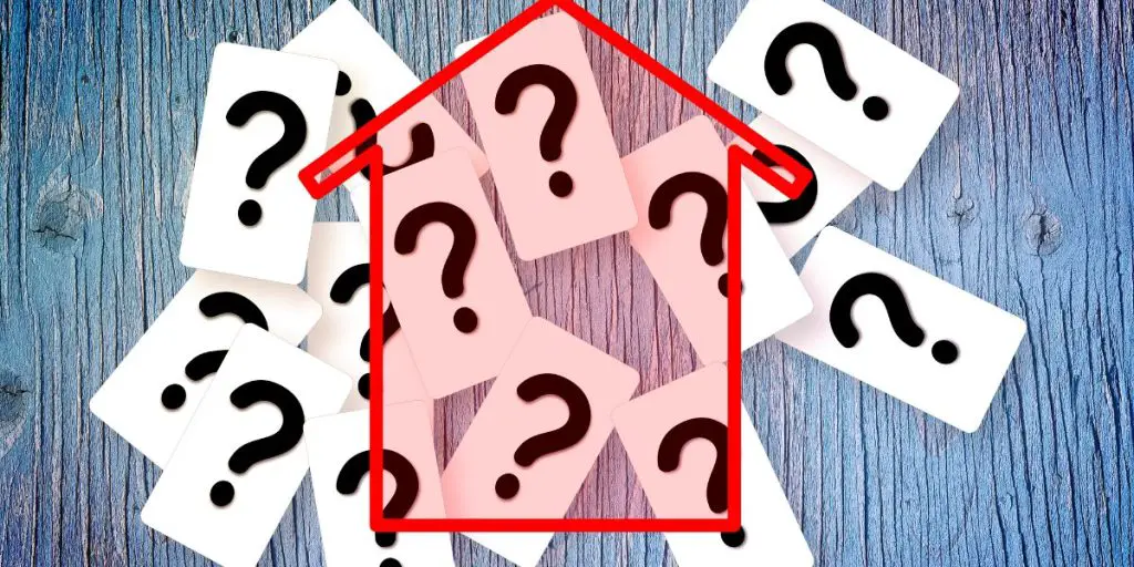 Several cards with question marks are arranged under a red outline of a house on a wooden surface, sparking curiosity about the perfect time to invest in a rental property.