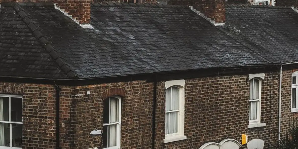 Row of brick terraced houses with dark slate roofs, white framed windows, and chimneys in overcast lighting—ideal for those investing in HMOs.